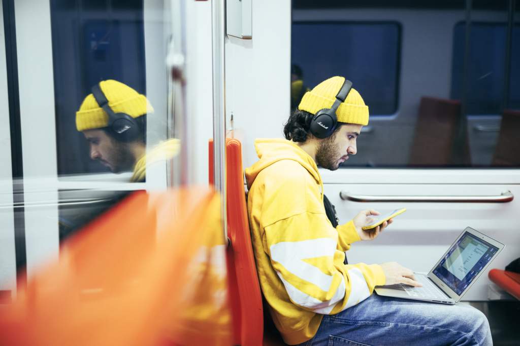 Matkustaja metrossa puhelimen ja tietokoneen kanssa