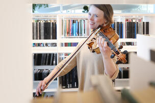 En kvinna spelar fiol framför bokhyllorna i biblioteket