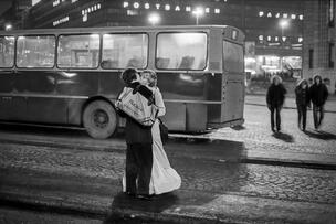Mustavalkoinen kuva, jossa mies ja nainen suutelevat, bussi taustalla.