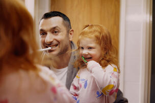 A parent and child brush their teeth together.