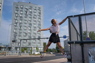 Henkilö temppuilee aitarakennelmassa kerrostalon edustalla.