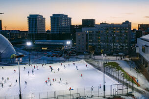 Ihmisiä luistelemassa ja pelaamassa jääkiekkoa valaistulla kentällä.