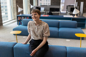 Maisema-arkkitehti Sofia Kangas nojaa hymyillen sohvaan työpaikkansa suuressa toimistohuoneessa, jossa on moderneja huonekaluja ja valaisimia. 