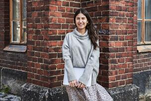 Nainen seisoo tiilirakennuksen edessä ja pitää käsissään kannettavaa tietokonetta, jonka kansi on suljettu.