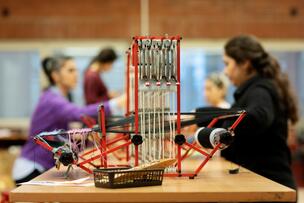 Small looms on the table, with people sitting around it in the background.