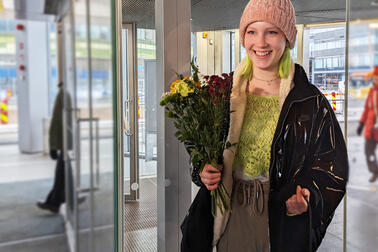 Oodi's ten millionth visitor Sonja in front of Oodi's doors with a bouquet of flowers in her hand.