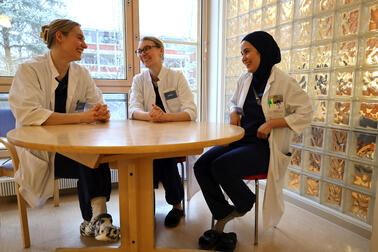 Erikoistuvat lääkärit Janita, Sofia ja Zahra istuvat pöydän ääressä ja juttelevat keskenään.