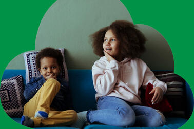 Two smiling children sit on a sofa.