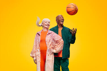 Two elderly people, one of whom is throwing a basketball into the air.