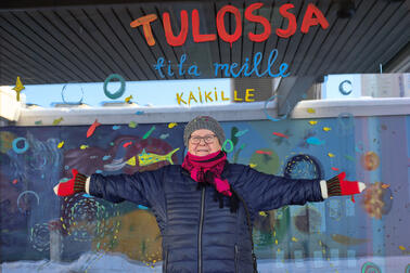 Liisa Aunula kädet sivuille avoinna värikkään ikkunan edessä.
