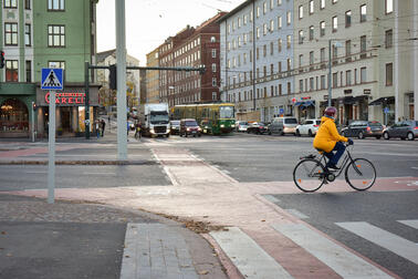 Suurten katujen risteys, jossa on pyöräilijä ja autoja liikennevaloissa