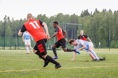 Fem personer spelar fotboll på gräs.