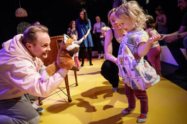 Actor plays with a hand puppet of a fox with a child.