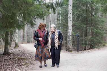 Two people walk on a dirt road in the woods.