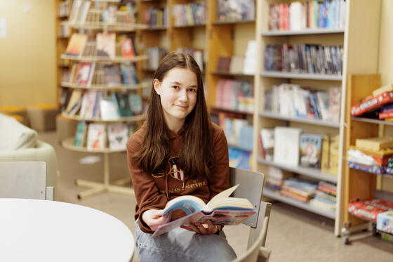 Vera Nylund sitter i Norsens skolbibliotek och bläddar i en bok.