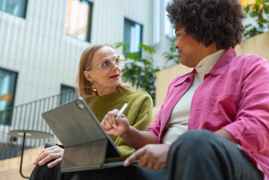 Kuvassa kaksi naista istuu rappusilla kannettavan tietokoneen kanssa.