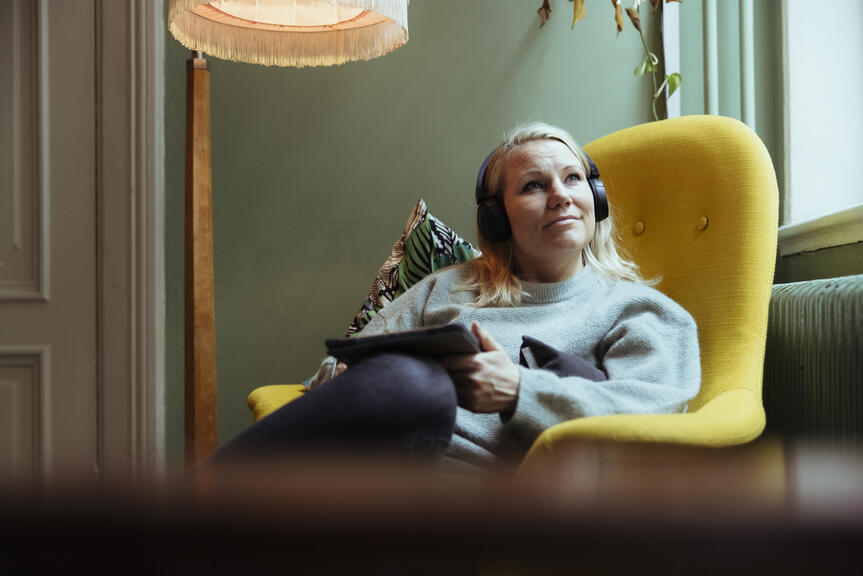 En kvinna sitter i en gul fåtölj med en skärm i handen.