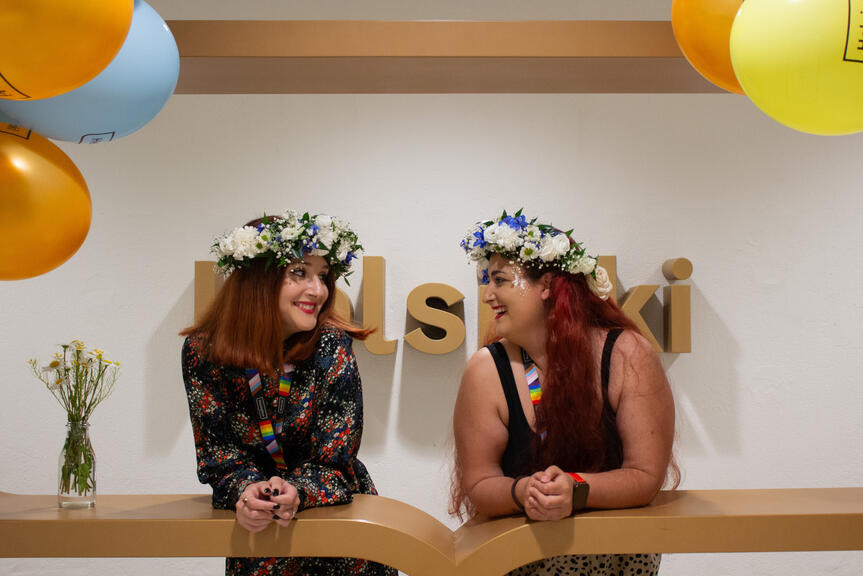Two smiling women with flowers in their hair at the City Hall's Helsinki logo