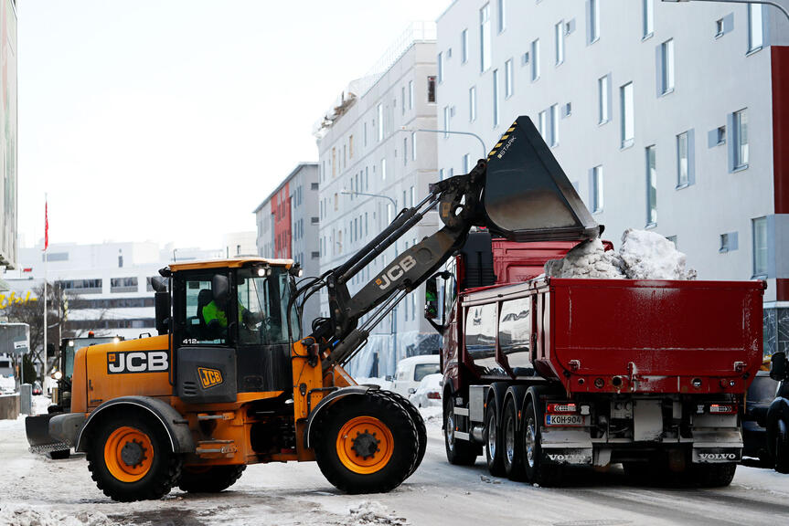 Traktori lastaa lunta kuorma-auton lavalle.