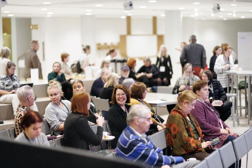 Representatives of organisations sitting side by side in the audience and talking to each other during an event. 