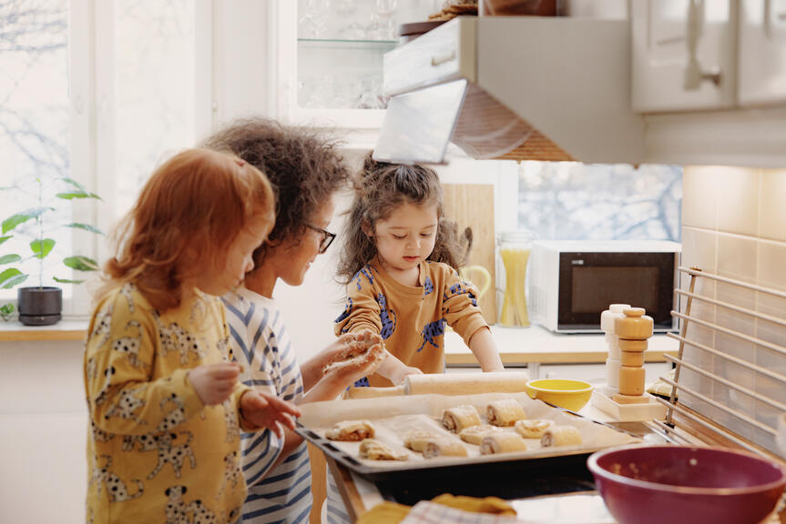 Kolme lasta osallistuu leipomiseen valoisassa keittiössä. 