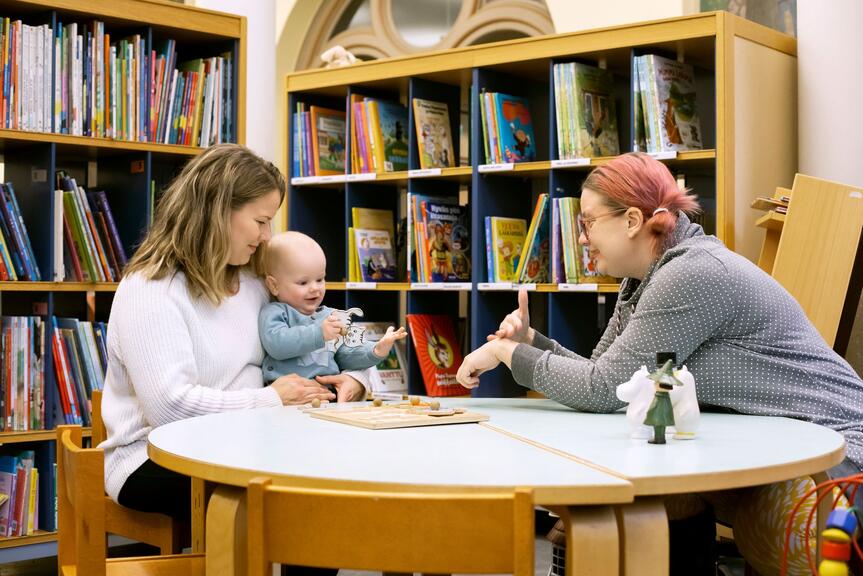 Two women and a baby sit at a table and talk using sign language.