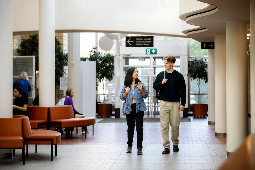 Två ungdomar går sida vid sida och pratar med varandra i entréhallen.