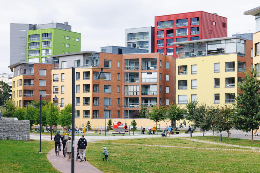 Perhe ulkoilemassa puistossa, taustalla näkyy kerrostaloja.