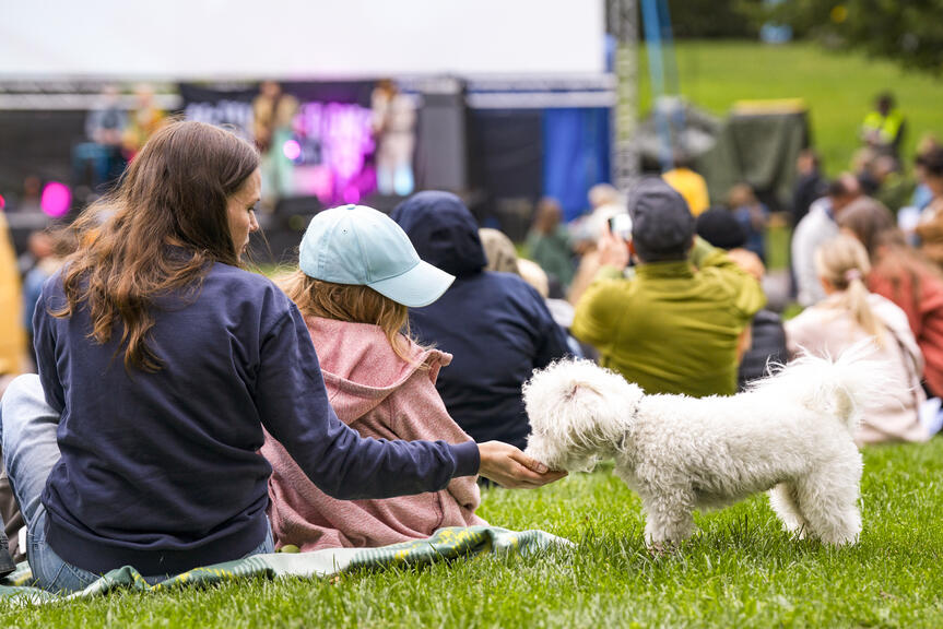 A woman and a child are petting a dog on the grass at the Kinokoffari event.