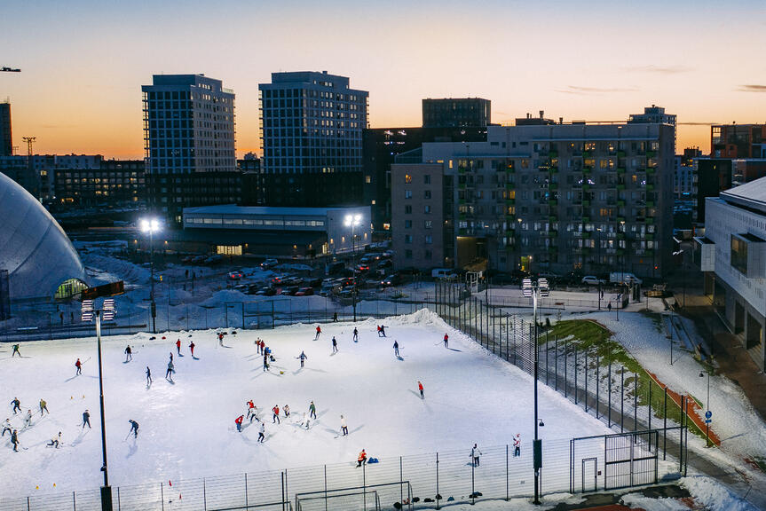 Ihmisiä luistelemassa ja pelaamassa jääkiekkoa valaistulla kentällä.