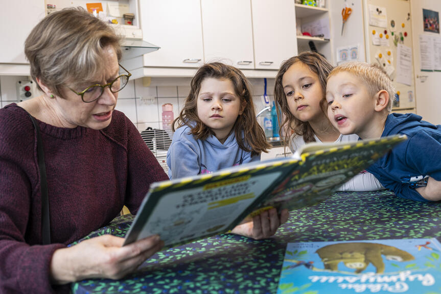 Aikuinen ja kolme lasta katsovat kirjaa.