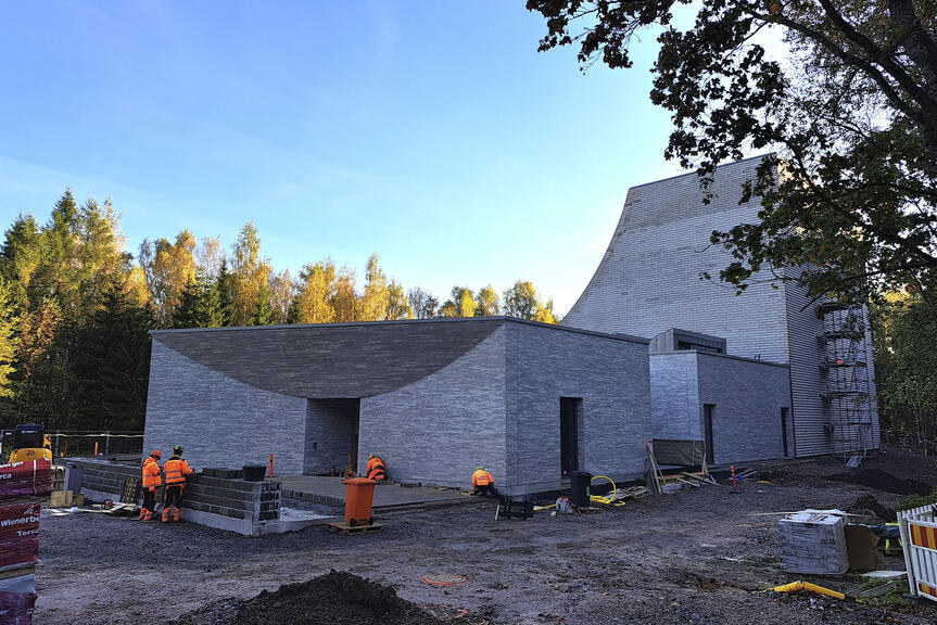Rakennustyömaa, jossa on vaalea kaarevalinjainen tiilirakennus ja rakennustyöntekijöitä