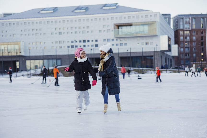 Kaksi nuorta henkilöä luistelemassa iloisina, toisella on kypärä päässä.