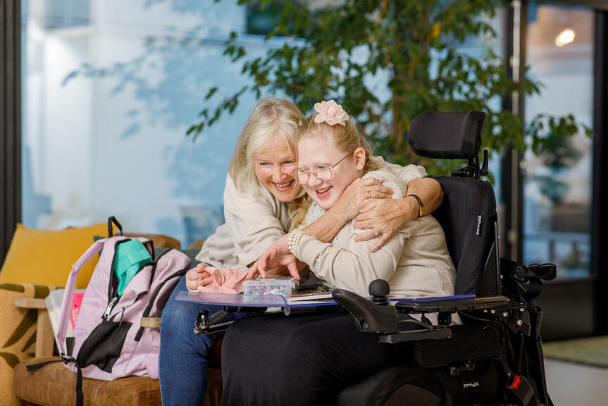 Nainen sohvalla ja tyttö pyörätuolissa halaavat