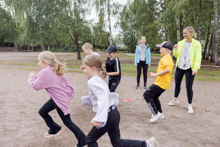 Barn springer utomhus tillsammans med ledaren.
