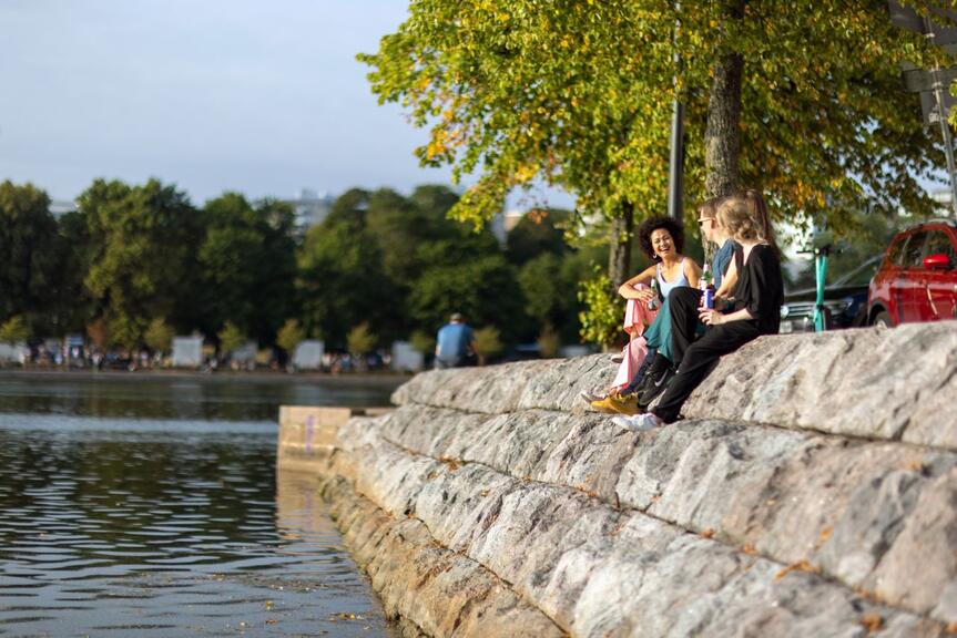 Folk sitter vid havet i solskenet.