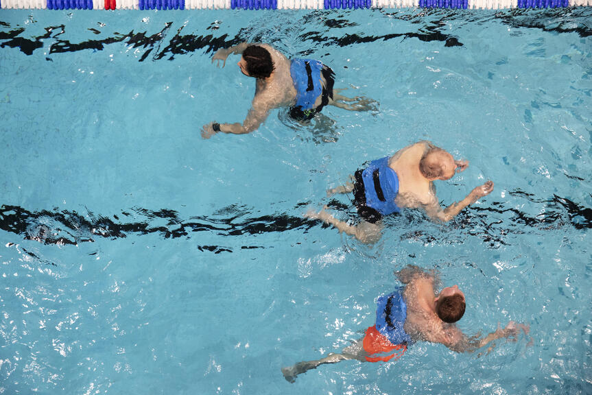 Tre personer som simmar i en bassäng fotograferade ovanifrån.