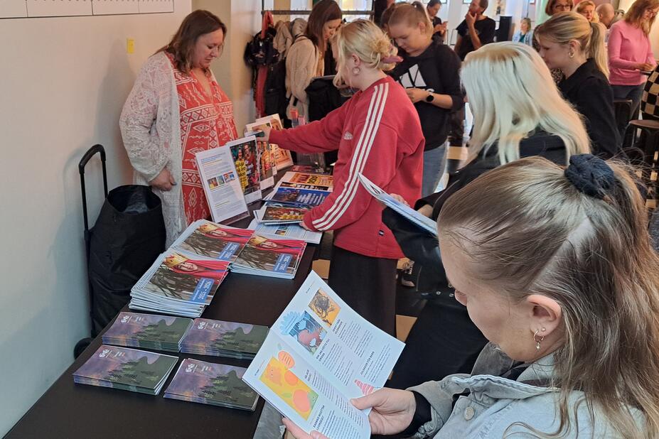 Människor samlas runt ett stånd för att bläddra i broschyrer.