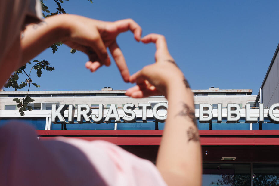Kontulan kirjaston nimikyltti ja ihminen, joka tekee käsillään sydämen.