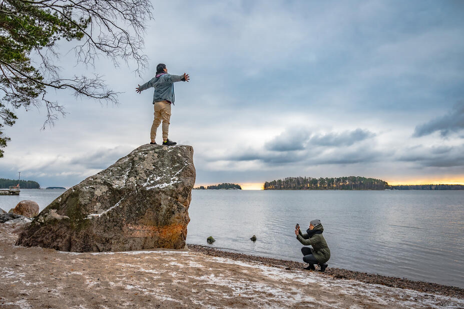 Henkilö kuvaa toista henkillö kivellä, taustalla meri.