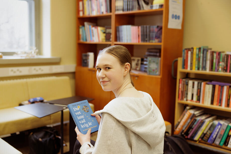 En elev ler mot kameran med boken "Du vet inte vad krig är" i handen.