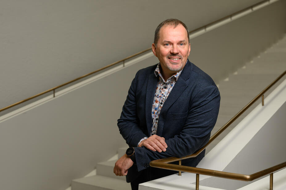 Henkilöstöjohtaja Petri Lumijärvi nojaa kaiteeseen kaupungintalon portaikossa ja katsoo kohti hymyillen.