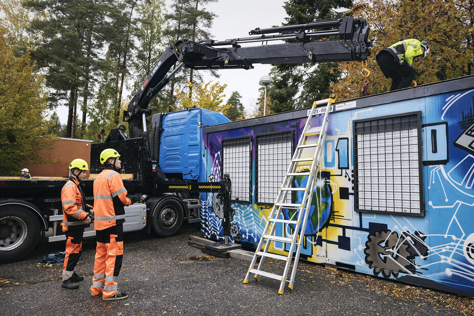 Opiskelijat katselevat, kun opettaja on kiivennyt kontin päälle tikapuilla..