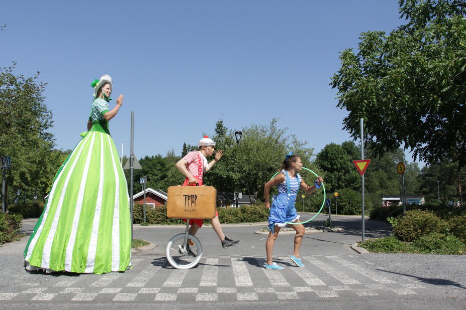 Circus artists with stilts, a unicycle, and a hoop.