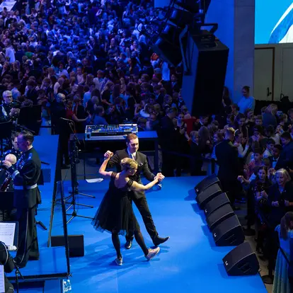 Two people dance on stage while children dance around them.
