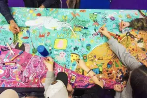 Children are drawing on a colourful tablecloth.