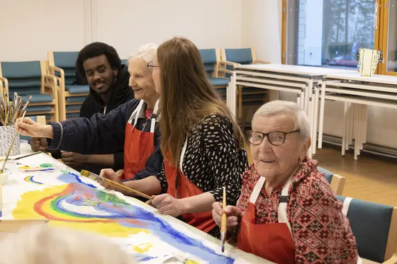 Kaksi työntekijää ja kaksi senioria maalaavat pöydän takana värikästä teosta.