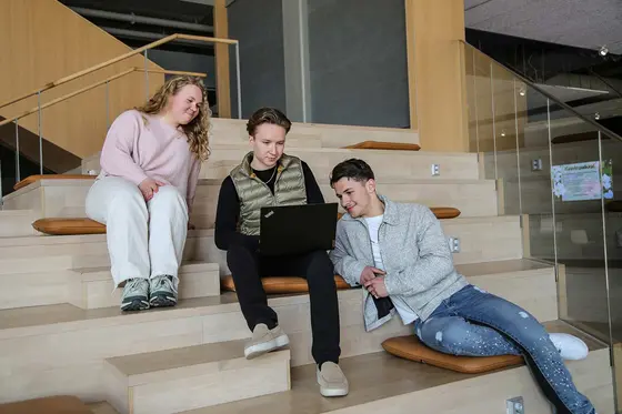 Opiskelijat istuvat rappusilla ja katsovat tietokonetta.