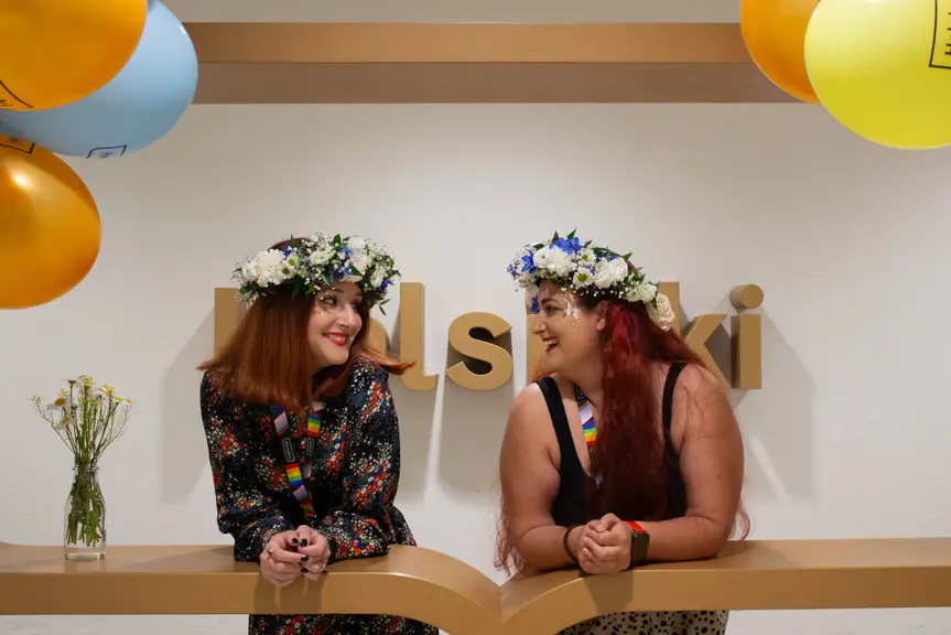 Two smiling women with flowers in their hair at the City Hall's Helsinki logo.