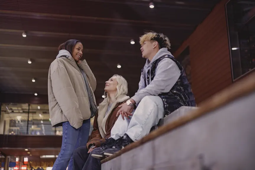 Three young people are talking together on outdoor steps.